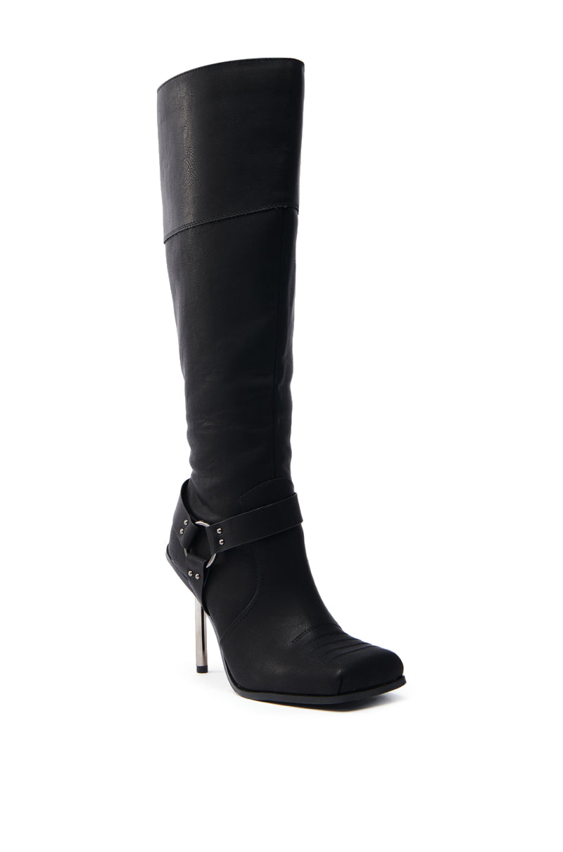The ELLERY BLACK STILETTO BOOT is a tall leather boot with a square toe and high heel. It features a decorative strap with silver studs near the ankle and has a knee-high shaft that stands upright, highlighting its sleek and elegant design.