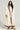 A person with long curly hair wearing the cozy BEAR HUG REVERSIBLE FLEECE TRENCH stands against a plain background. The oversized silhouette complements their light, casual clothing and tan boots, creating an effortlessly chic look.
