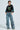 A person with short hair wears the CHAMPIONSHIP SCRUNCH JERSEY, a black crop top featuring varsity stripes and the number 13, paired with wide-legged cargo jeans. They stand confidently with one hand in their pocket against a plain background.