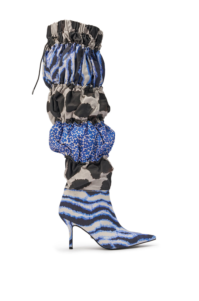 The AKIRA GOLD ELODIE BLUE MULTI PATCHWORK BOOT is a knee-high, slouchy stiletto with a pointed toe, featuring bold blue, black, and white animal prints and ruched patchwork sections along the shaft. 3