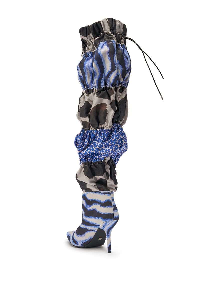 The AKIRA GOLD ELODIE BLUE MULTI PATCHWORK BOOT is an over-the-knee, high-heeled stiletto with a pointed toe, blue and black animal print patchwork, ruched slouchy sections, and a drawstring detail at the top. 5