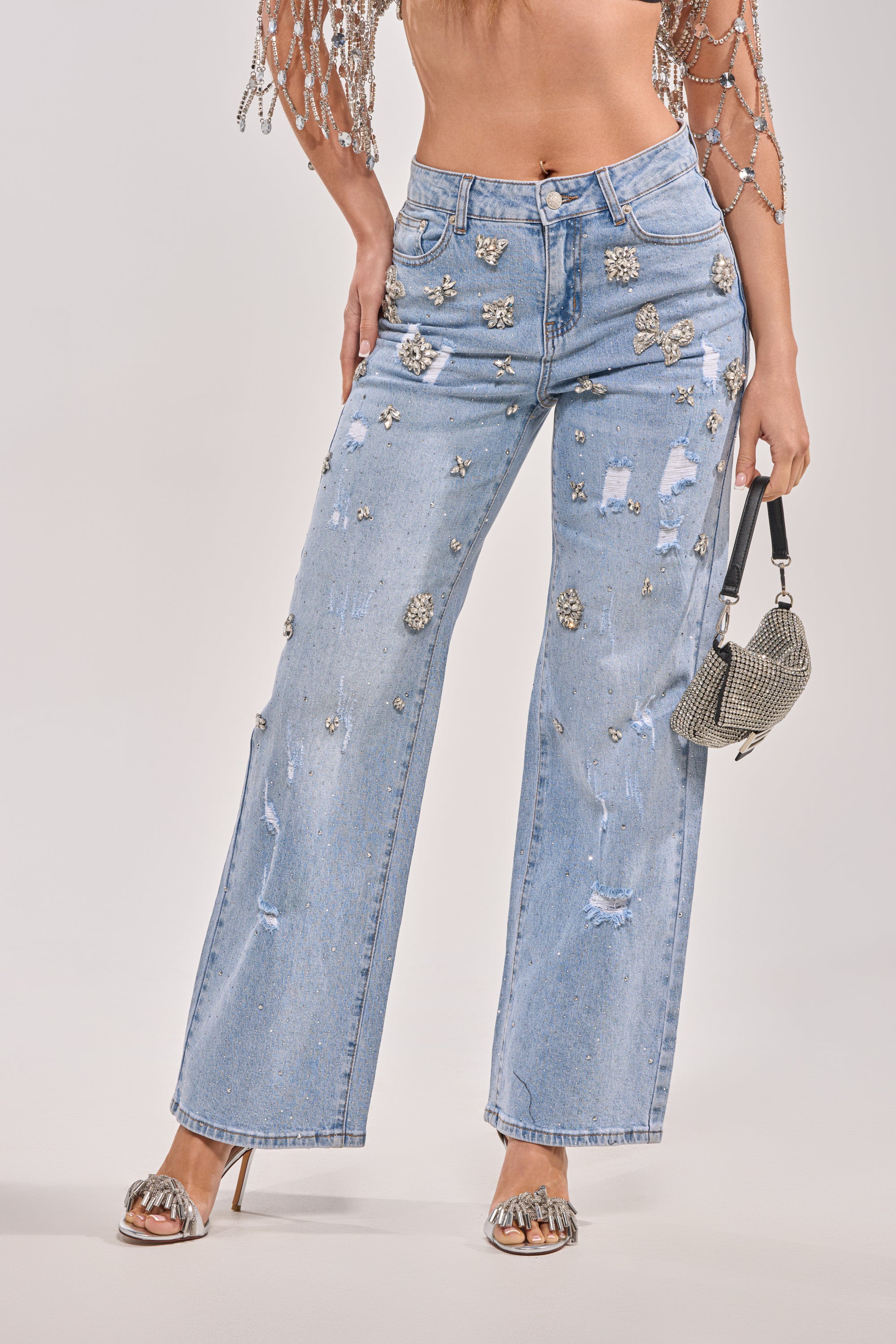 Wearing IN YOUR DREAMS RHINESTONE DENIM jeans with rips, styled with silver heels and a small silver handbag. Only the lower half of the person is shown. 2