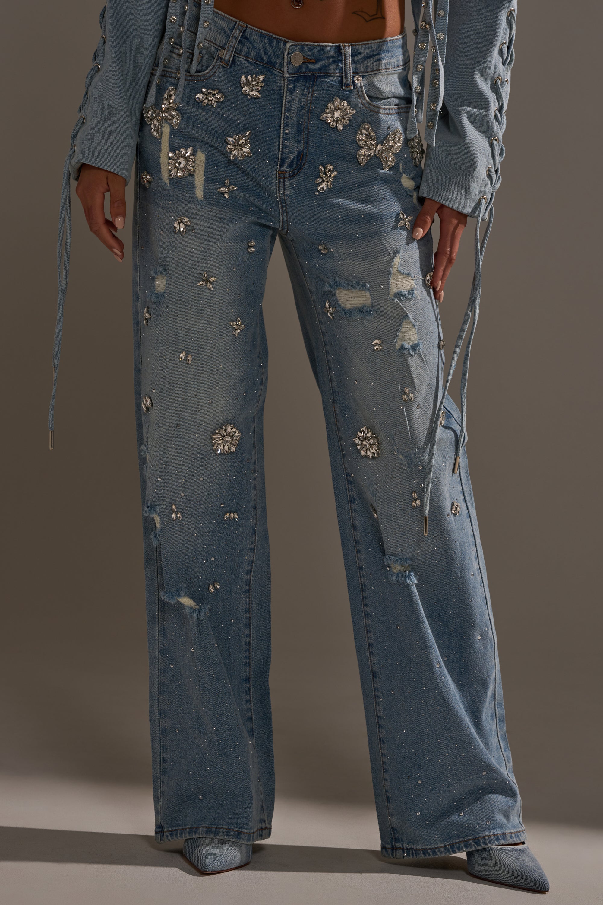 Wearing the IN YOUR DREAMS RHINESTONE DENIM JEANS with a relaxed, wide-leg fit and sparkling rhinestones, styled with a matching denim jacket featuring lace-up sleeves.