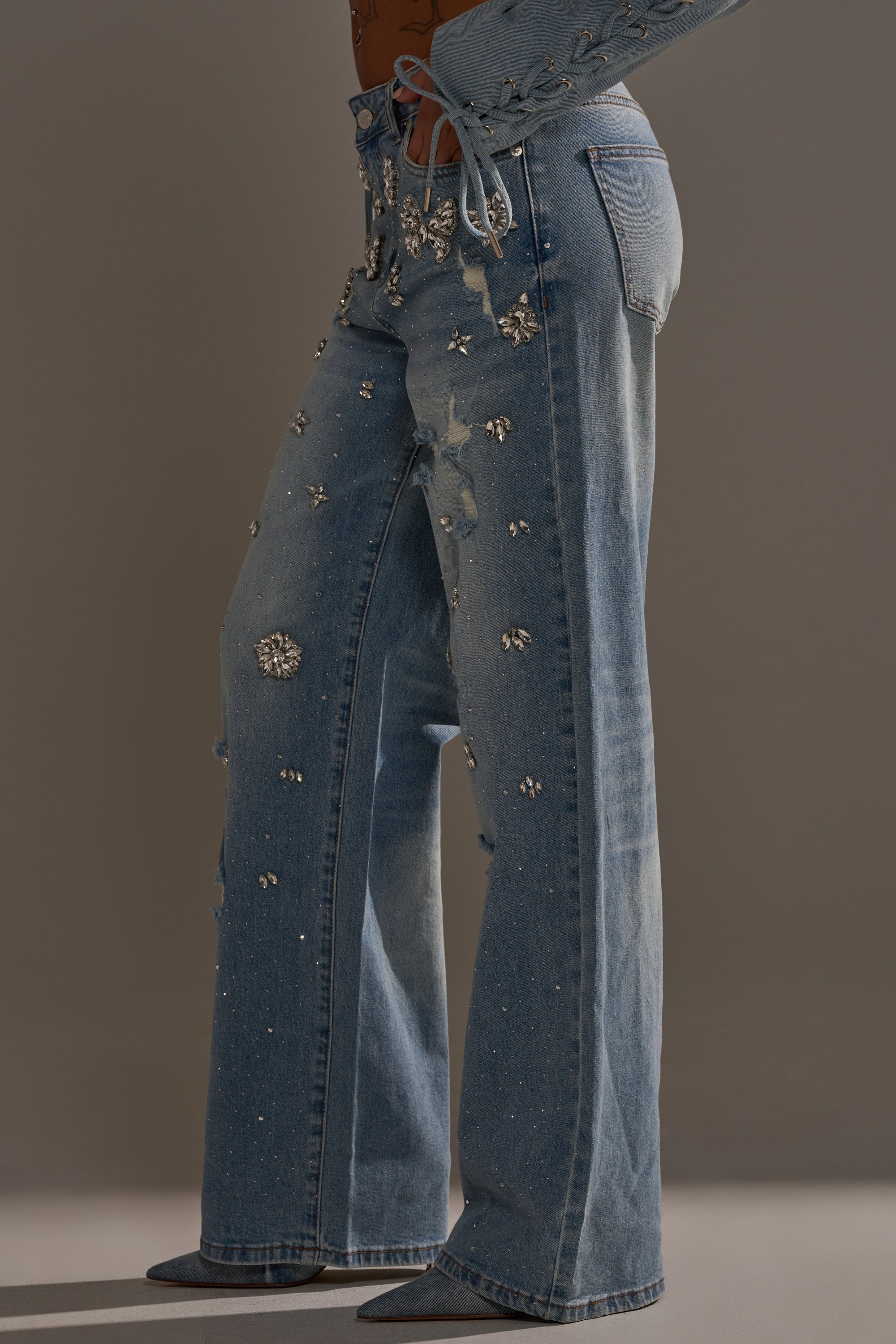 The IN YOUR DREAMS RHINESTONE DENIM JEANS, featuring wide legs and sparkling rhinestone embellishments, are modeled against a neutral background, showing only the lower body and part of the midriff.