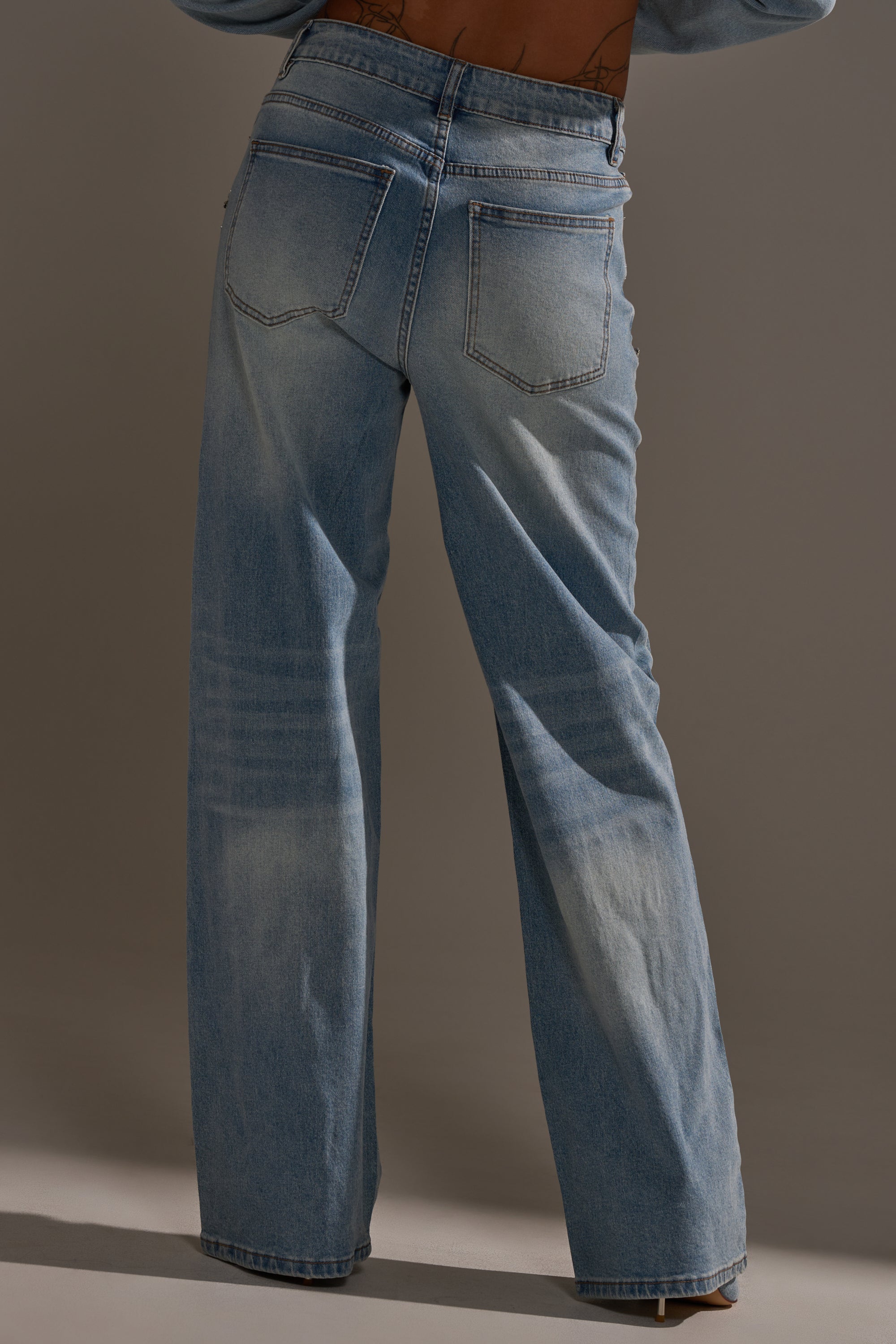 Person shown from the back wearing IN YOUR DREAMS RHINESTONE DENIM JEANS in light blue, featuring high waist, wide leg cut, visible pockets, and subtle thigh and knee fading against a neutral background.
