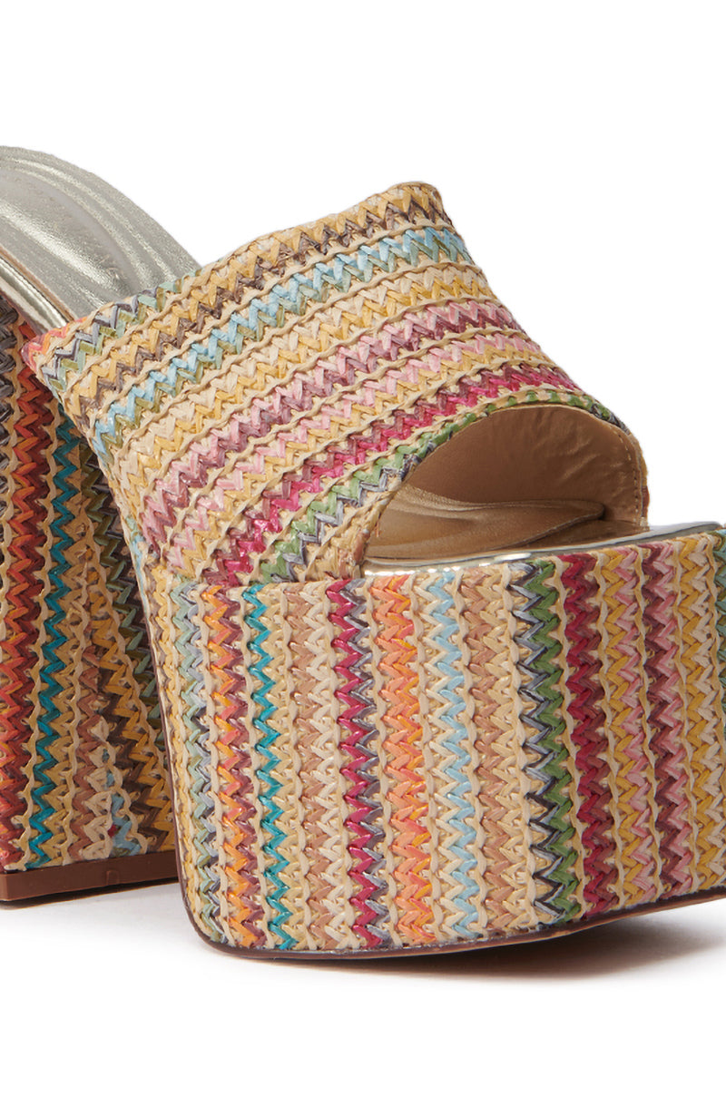 The AZALEA WANG EMBERS MULTI CHUNKY PLATFORM SANDAL features a close-up of a chunky heeled sandal with an open toe, raffia upper, and vibrant multicolored zigzag pattern in red, yellow, blue, and green for added flair.