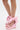 A person wearing the AZALEA WANG EMEKA Pink Platform Sandal with Bow, featuring pink faux leather wedge heels and large ribbon ankle bows, stands on a white background.