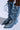 The AZALEA WANG EMMALINE DENIM STILETTO BOOT features knee-high shafts, pointed toes, and intricate lace-up detailing. The laces extend fully, creating an elaborate pattern. With small curved heels and a denim finish, they offer a stylish and casual look.