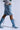 Striding confidently against a plain background in knee-high AZALEA WANG EMMALINE DENIM STILETTO BOOTS and a matching skirt, paired with a colorful top, the outfit exudes a casual yet trendy vibe that skillfully elevates classic denim with bold style choices.