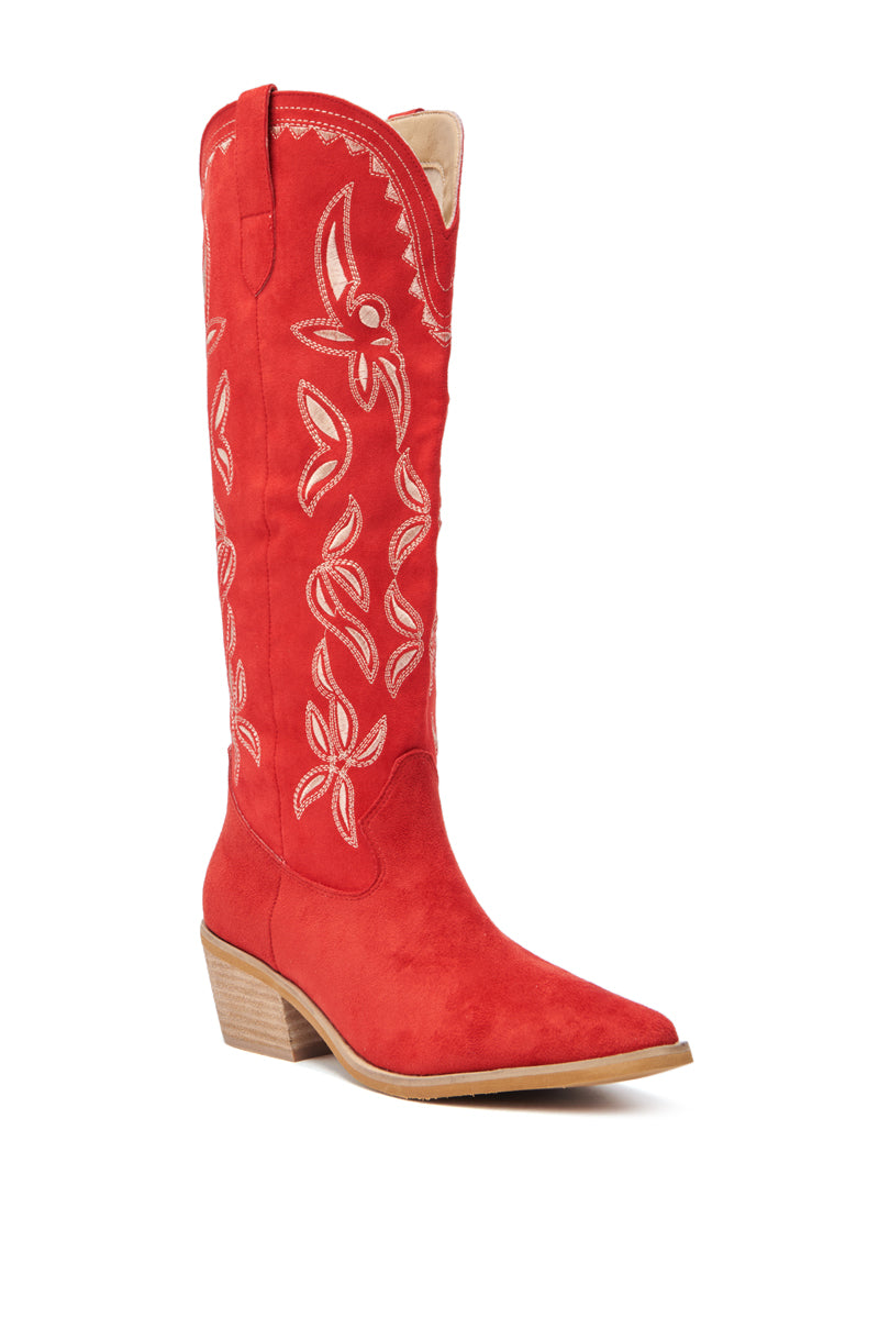 The ENORA RED KNEE HIGH COWBOY BOOT features red faux suede, a pointed toe, tan stacked heel, and white embroidered floral cowboy stitching along the shaft.