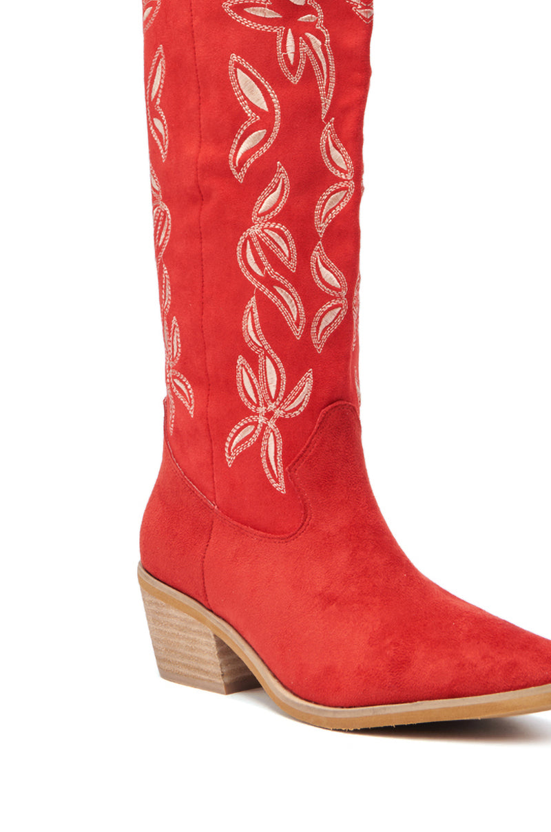 The ENORA RED KNEE HIGH COWBOY BOOT features red faux suede, a tan wooden heel, and bold white floral cowboy stitching along the shaft.