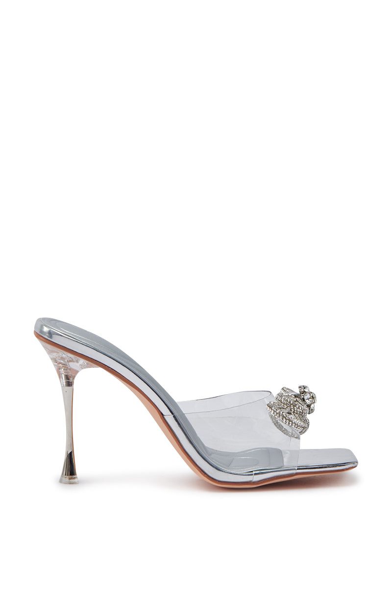 The AZALEA WANG ENTRANCING SILVER DIAMOND BOW DETAIL SANDAL features a clear high-heeled mule design with a pointed toe, rhinestone strap, sparkling silver diamond bow, slim stiletto heel, and a glossy sole for an elegant finish.