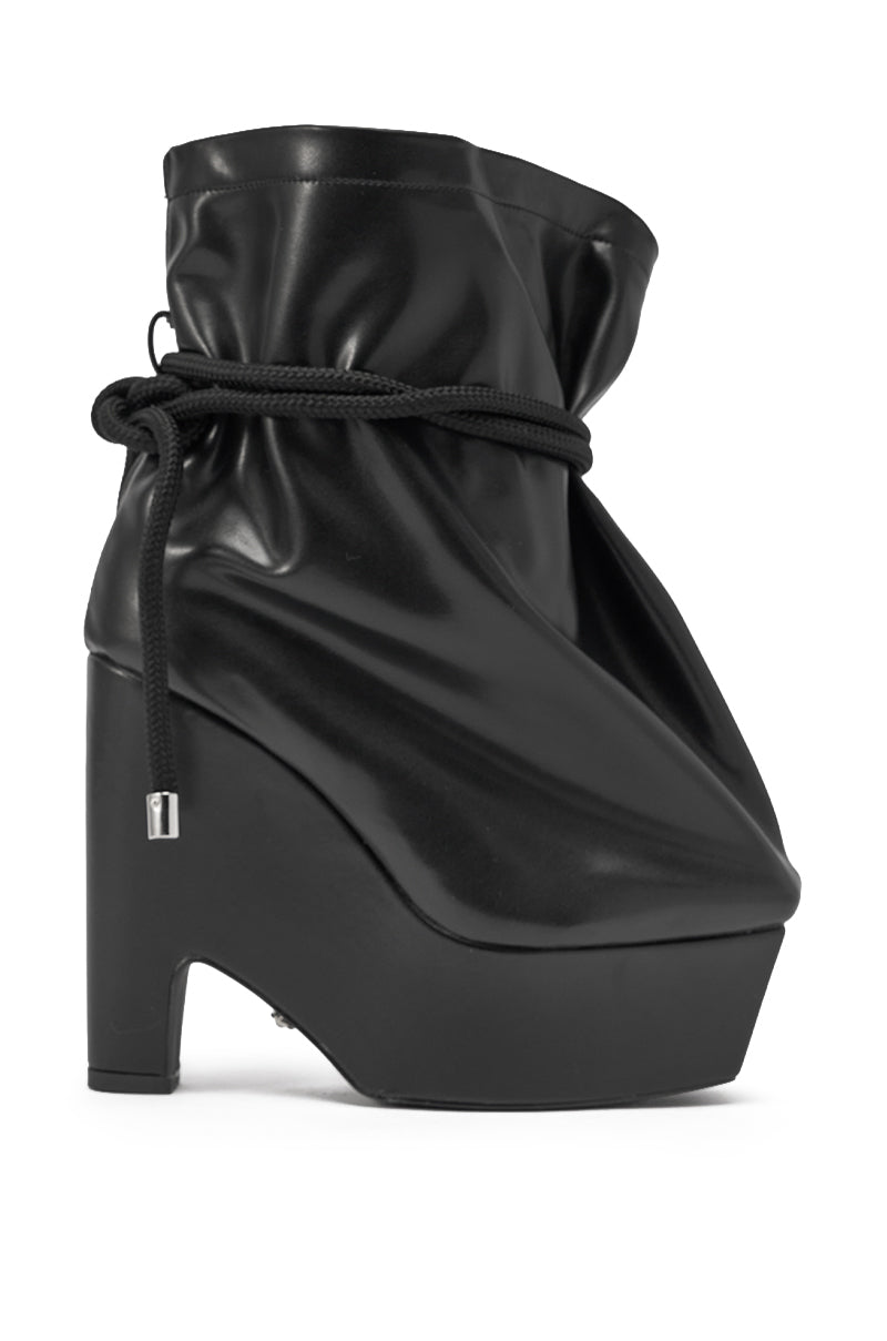 The AKIRA GOLD EPIGRAM PU Slouch Chunky Heel Bootie is a black faux leather bootie with a glossy, slouchy upper, high block heel, platform sole, and an ankle cinched by a black cord tied at the side. 3