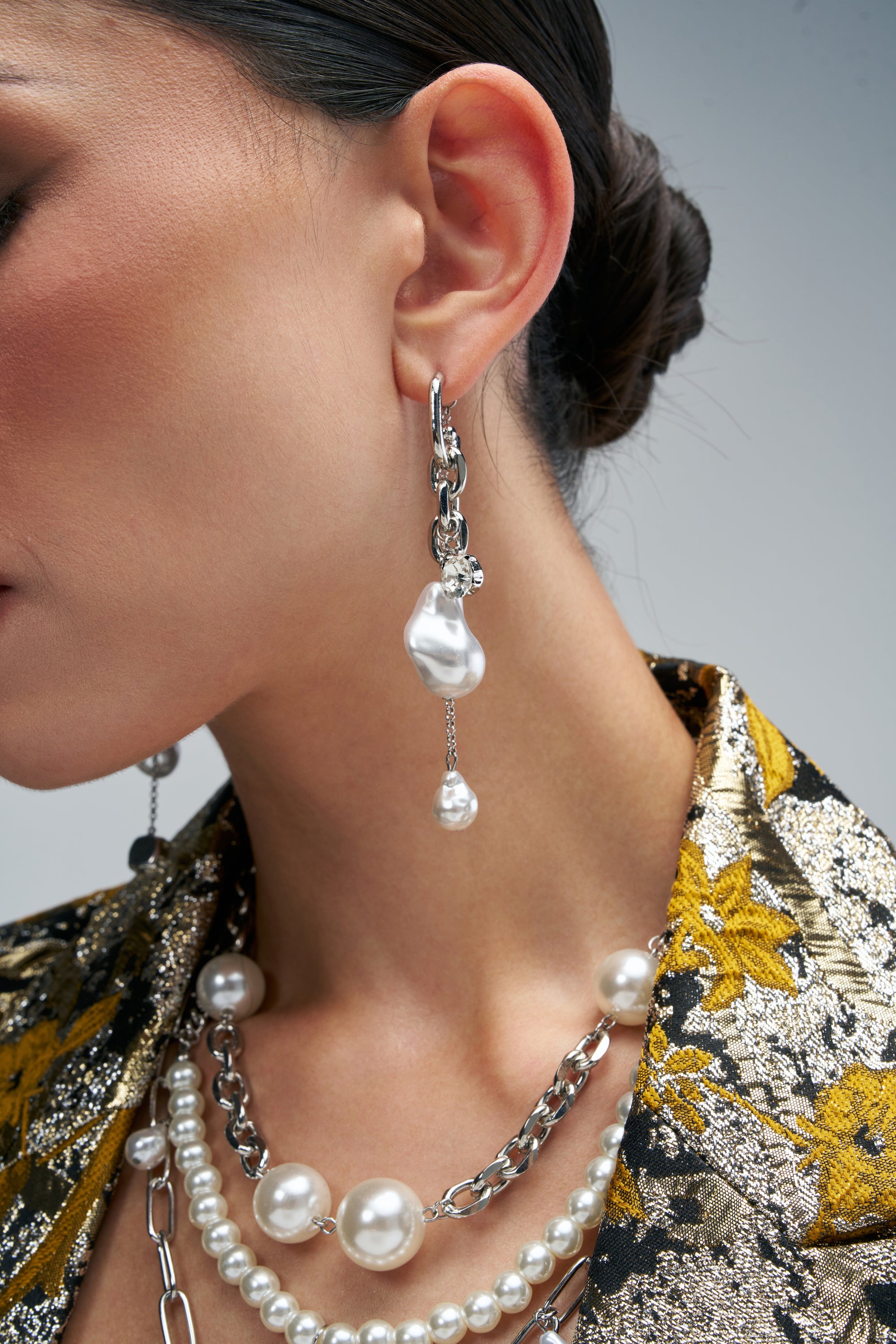 A person wearing IT GIRL PEARL EARRINGS, featuring long silver statement chain-links with an asymmetrical baroque pearl and a small dangling round pearl.