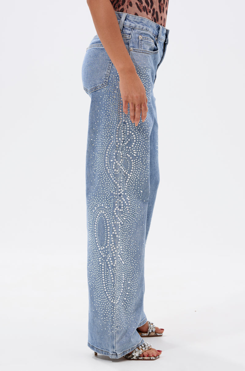 Someone wears the DREAMING OF YOU WIDE LEG DENIM—light blue high-rise jeans with rhinestone and white side designs—paired with a leopard print top and sparkly open-toe heels against a plain white background. 2