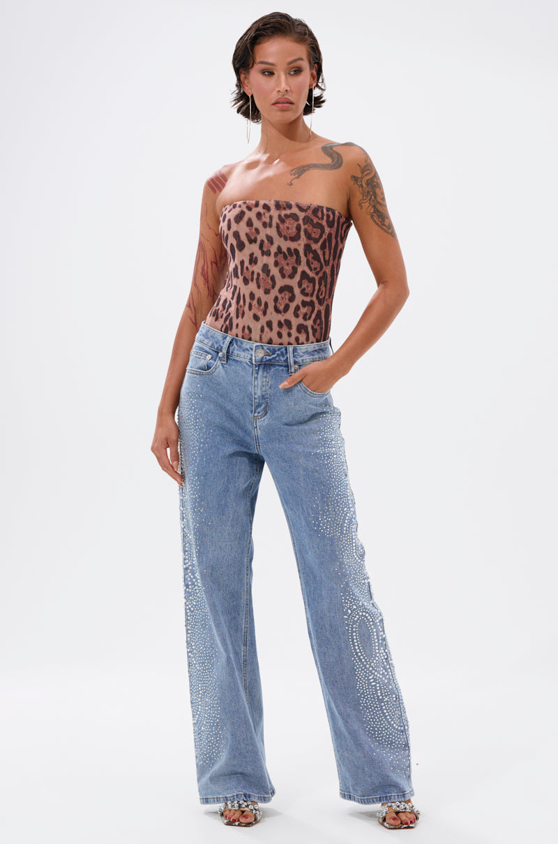 A woman with tattoos and short wet-look hair stands against a white background, wearing a leopard print strapless top and DREAMING OF YOU WIDE LEG DENIM rhinestone jeans in a light blue wash, paired with sandals. 5