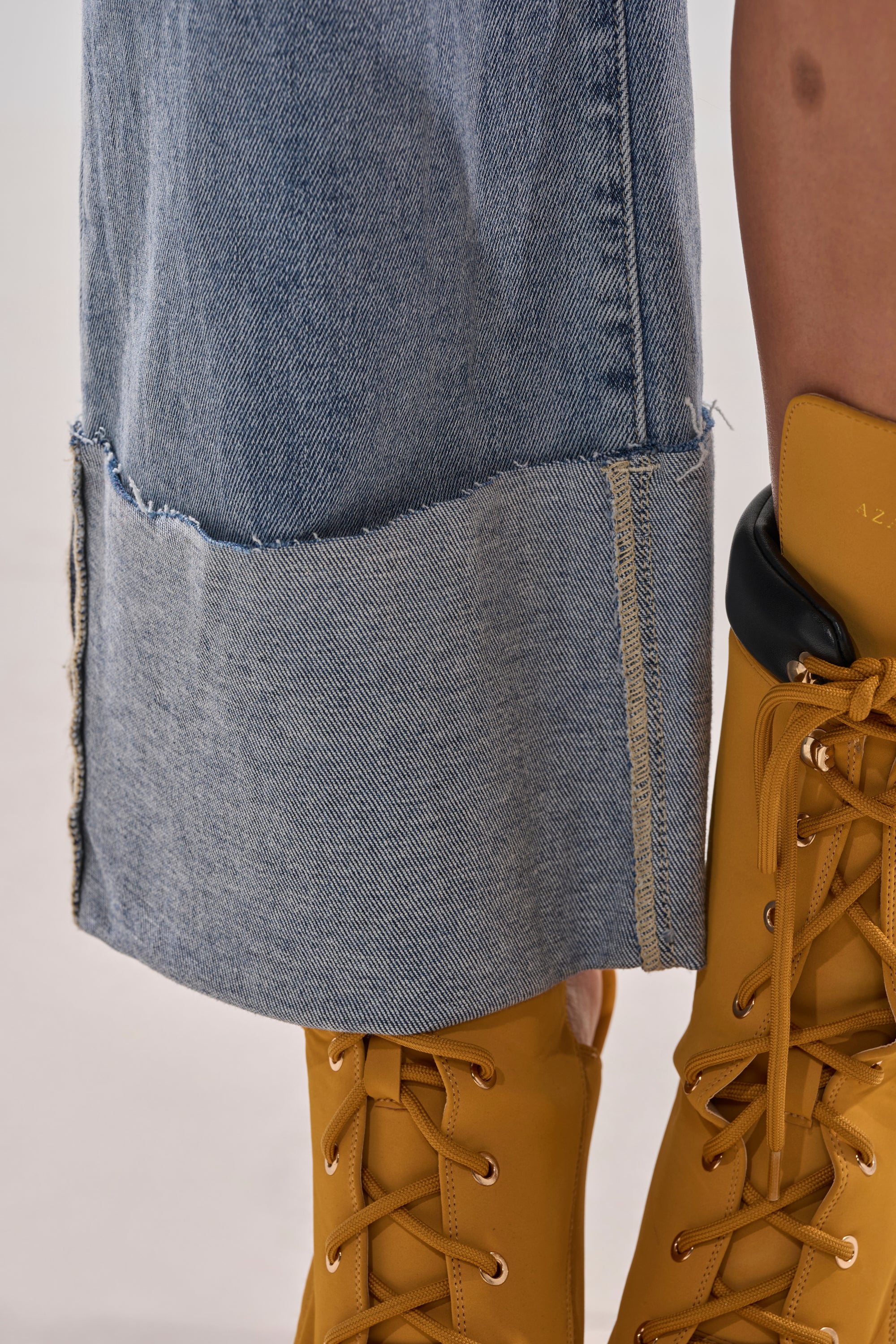 Close-up of lower legs wearing BOTH SIDES OF ME DENIM—light-wash, wide-leg jeans with a mismatched raw hem and visible stitching for a casual look—paired with yellow lace-up boots.