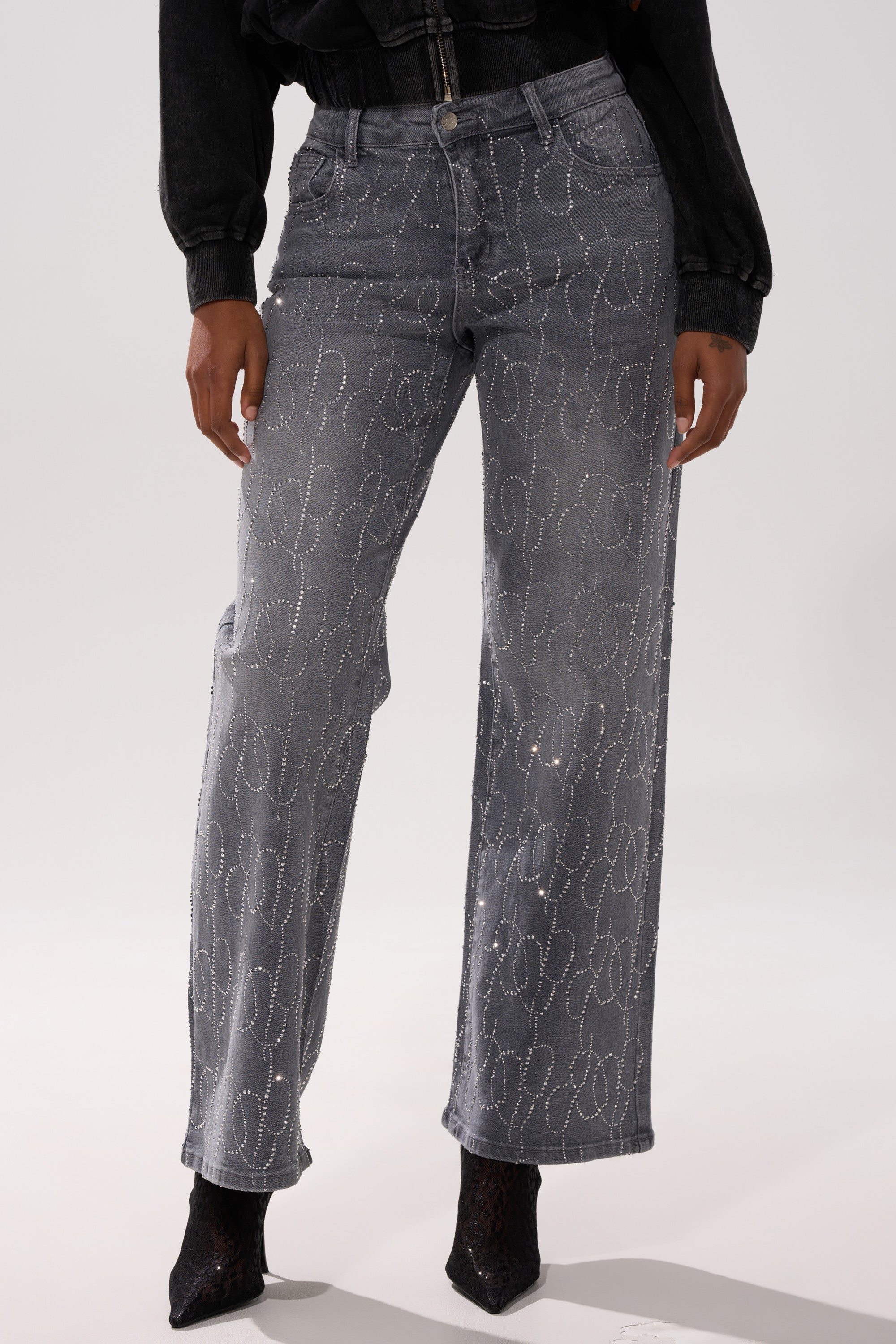 Wearing the PERFECT LIKE ME EMBELLISHED DENIM—high-rise straight-leg jeans with a silver rhinestone swirl—a person pairs them with a black top and pointed-toe shoes, standing against a plain light background.
