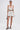 A woman faces forward in a white halter crop top and the CUTIE PIE RUFFLE HEM MINI SKIRT with black wavy piping, styled with strappy black heels, a small black purse, hoop earrings, and slicked-back hair against a white background.