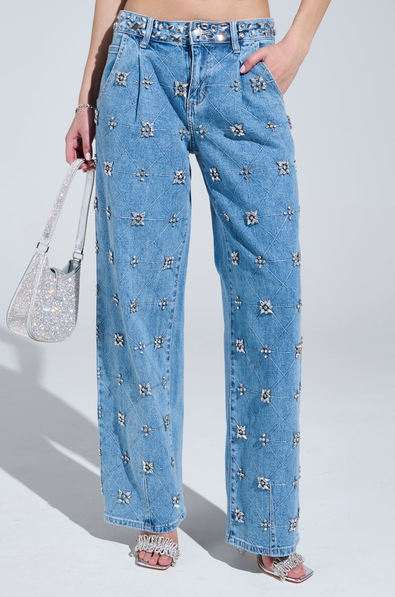 Wearing TAKE ME OUT RHINESTONE DENIM JEANS with a diamond-shaped rhinestone pattern, paired with a glittery handbag and heeled sandals for added sparkle.