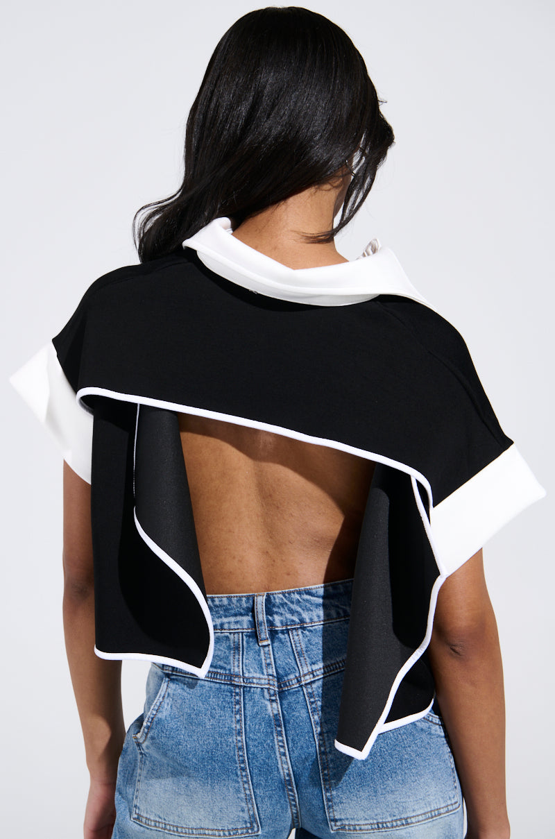A person with long dark hair faces away from the camera, wearing the NOTHING TO SEE BLOUSE. This backless black and white AKIRA Label top has a unique draped design and exposed lower back, perfectly paired with high-waisted blue jeans. 3