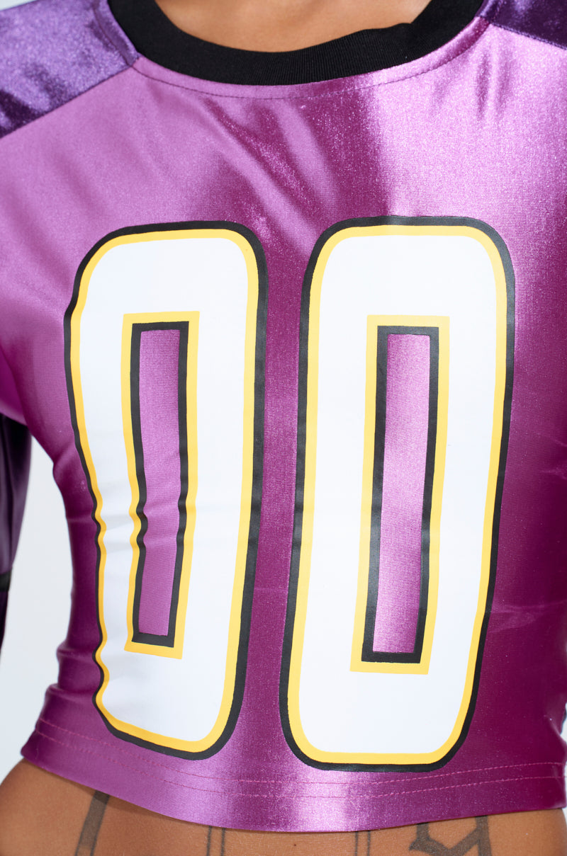 A person wore the DOUBLE ZERO JERSEY, flaunting a purple design with "00" in bold white and yellow. The jersey features a black neckline and bright purple sleeves, exuding an athletic yet chic style. Only the torso is shown in the image.