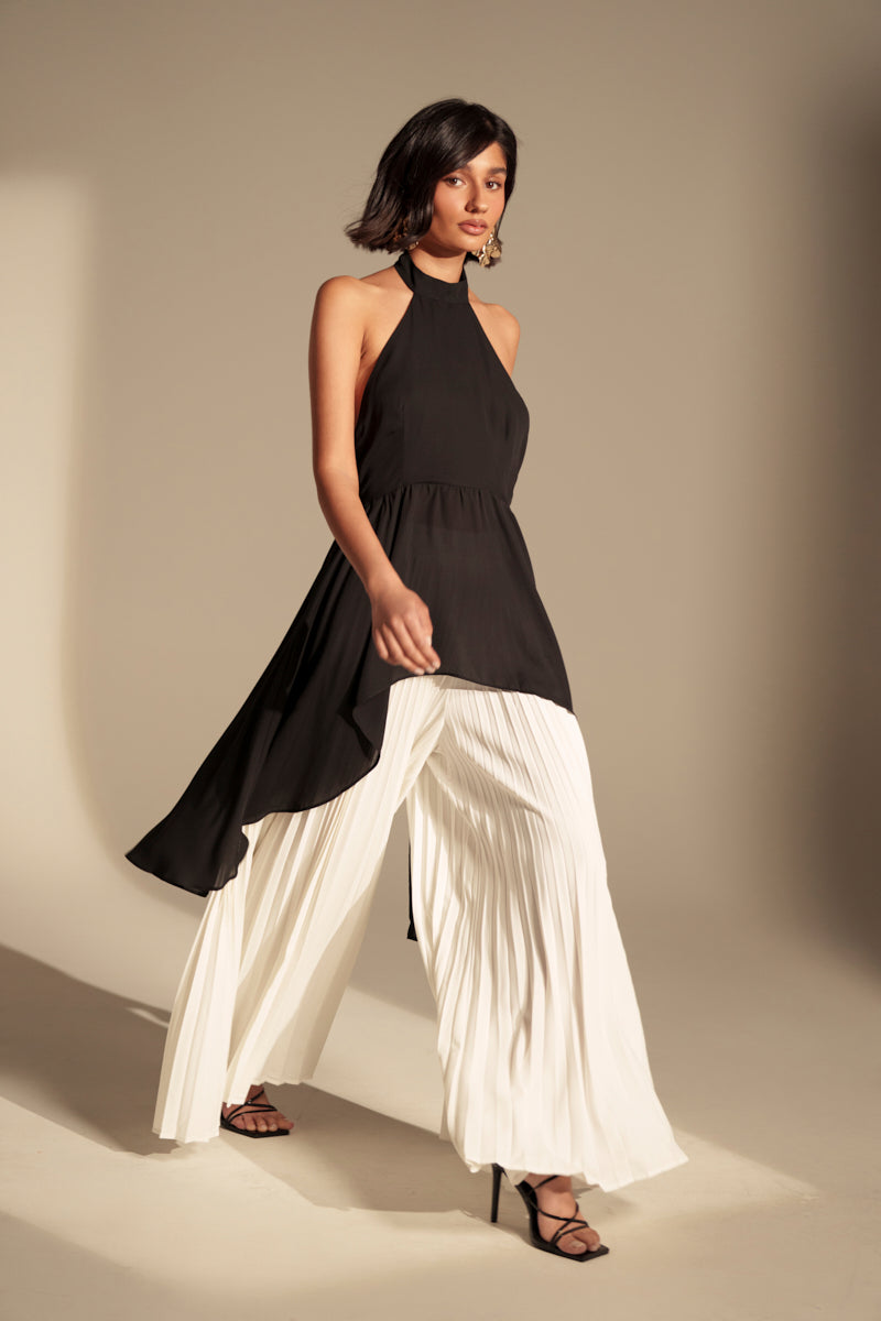 A woman wearing a sleeveless black halter top and the FLY INTO THE AIR PALAZZO PANT strides confidently in high-heeled sandals against a neutral background.