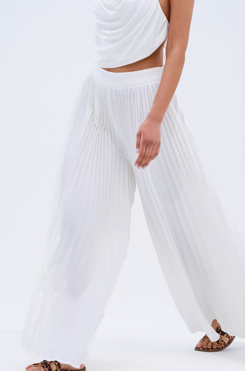 A person in FLY INTO THE AIR PALAZZO PANT and a white draped top walks forward, their face unseen. Pointed animal-print flats finish the look against a plain white background.