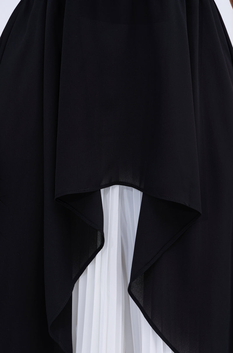 Close-up of the FLY INTO THE AIR BLOUSE, featuring a sleeveless black high neck outer layer with an asymmetrical hem draped over a white pleated chiffon blouse, highlighting a striking contrast in color and texture.
