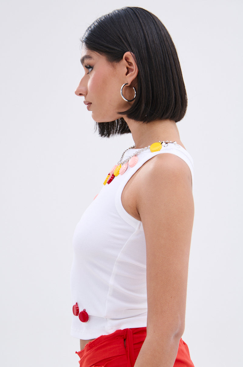 Woman with straight, chin-length dark hair wears the GIRL POWER TANK in white ribbed knit, paired with red pants, hoop earrings, and a colorful beaded necklace, shown in profile against a plain light background.