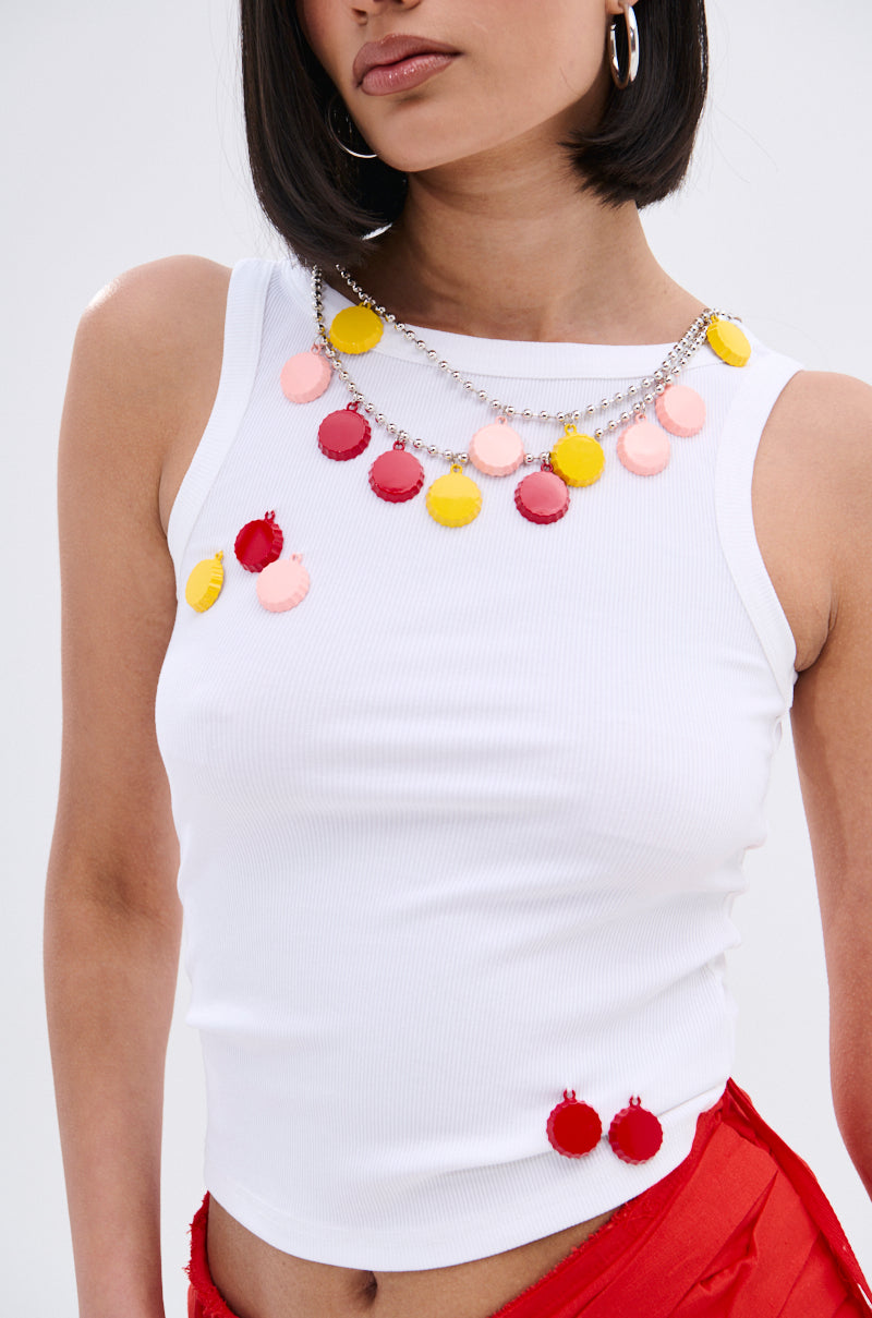 A woman wears the GIRL POWER TANK in white ribbed knit with red bottoms, accessorized with a chunky necklace and earrings featuring round pink, red, and yellow pendants. Only her upper body is visible.