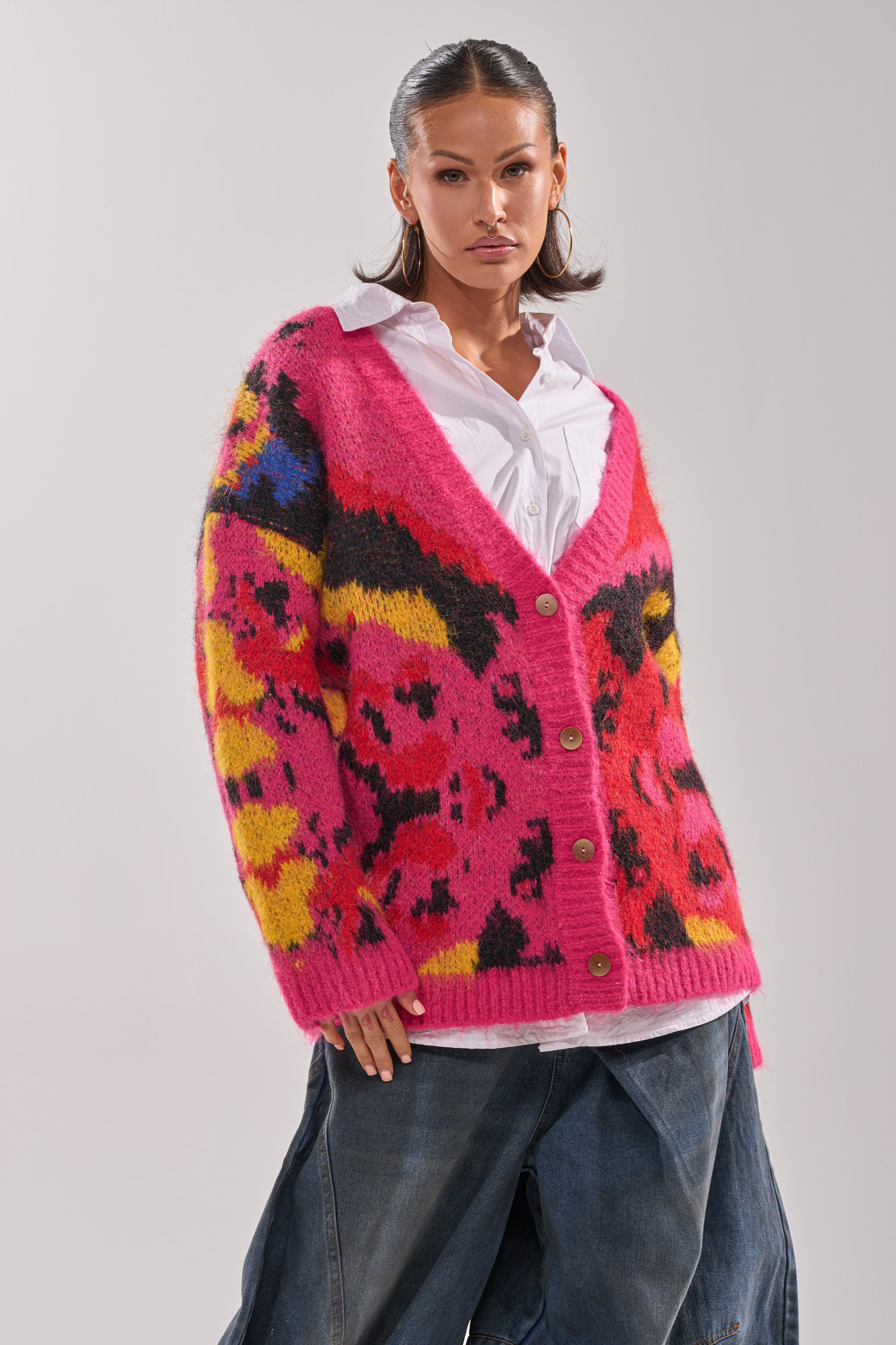 A woman models the COZY VIBES CARDIGAN—a vibrant, multi-color layer—over a white shirt and loose denim pants, set against a plain light background.