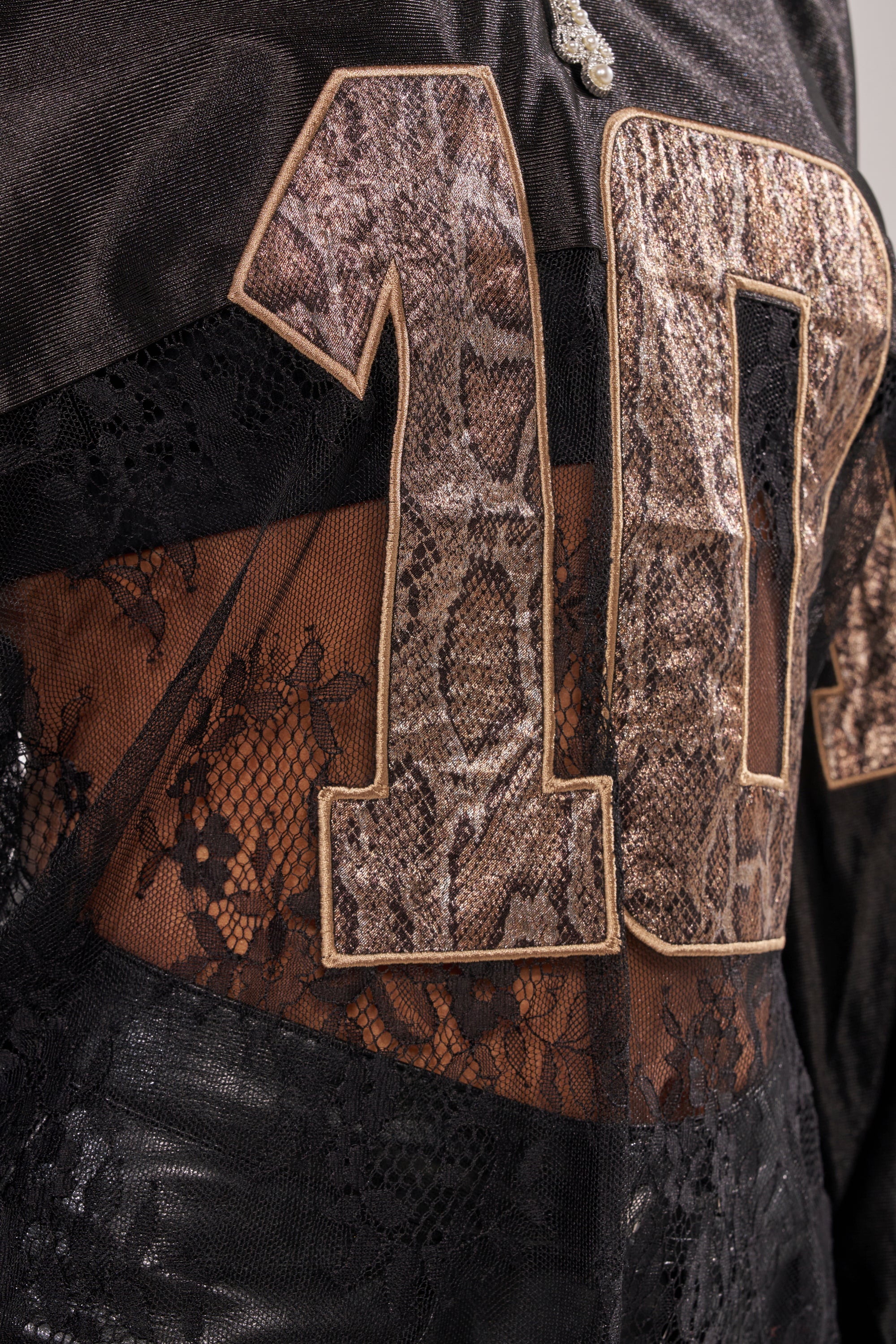 Close-up of the ROCKY LACE JERSEY, an oversized top with black lace, sheer panel, and a varsity "10" in brown snakeskin pattern sewn on for streetwear style. 9