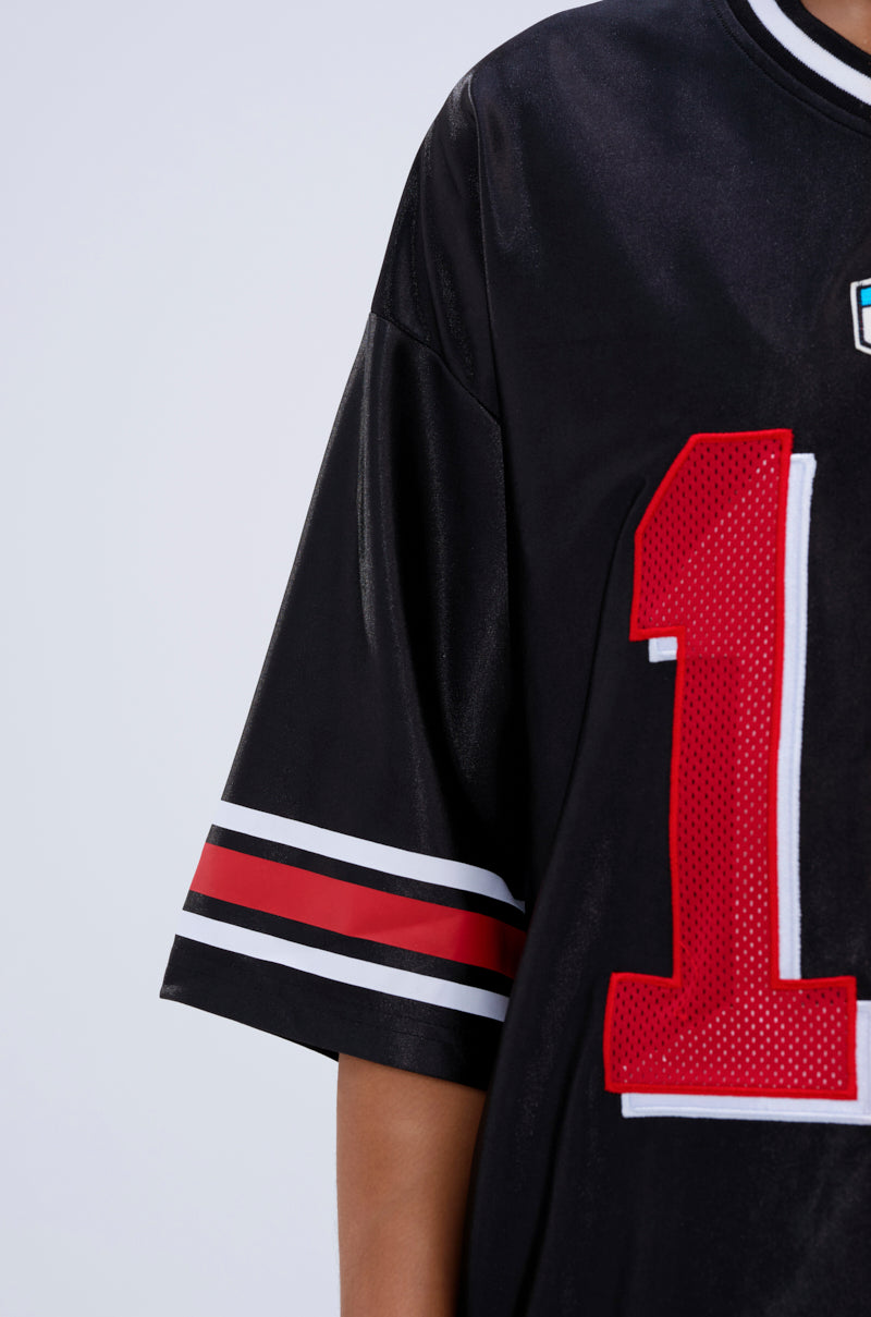 A close-up of a person wearing the SPLIT PERSONALITY JERSEY TOP—an oversized, color block tee in black with red and white sleeve stripes and a bold red "1" on the front. Only the upper torso and arm are visible.