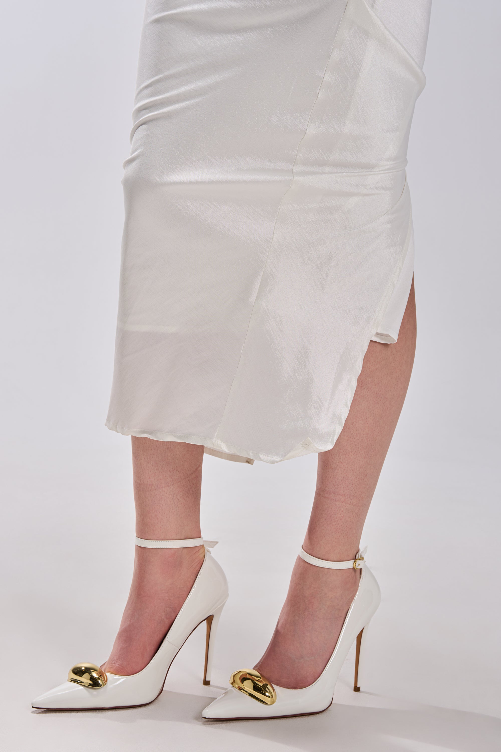 A person wearing a silky white midi skirt and the AZALEA WANG ESMARIA WHITE METAL EMBELLISHED PUMP with stiletto heels stands against a plain white background.