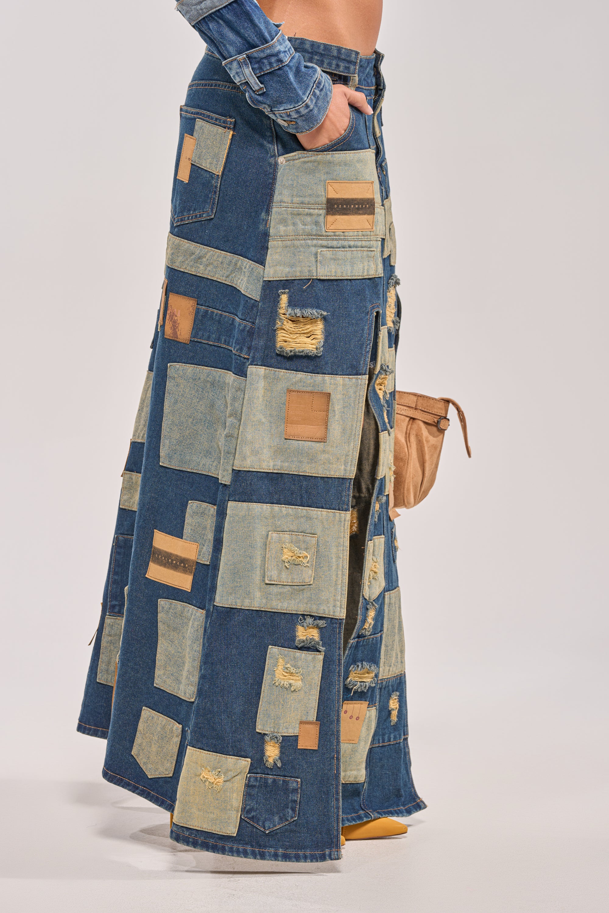 Only the lower body is visible, wearing the PATCH ME UP DENIM MAXI SKIRT with its mixed denim shades and textures, styled with a small tan bag and yellow shoes—ideal for streetwear or festival looks. 3