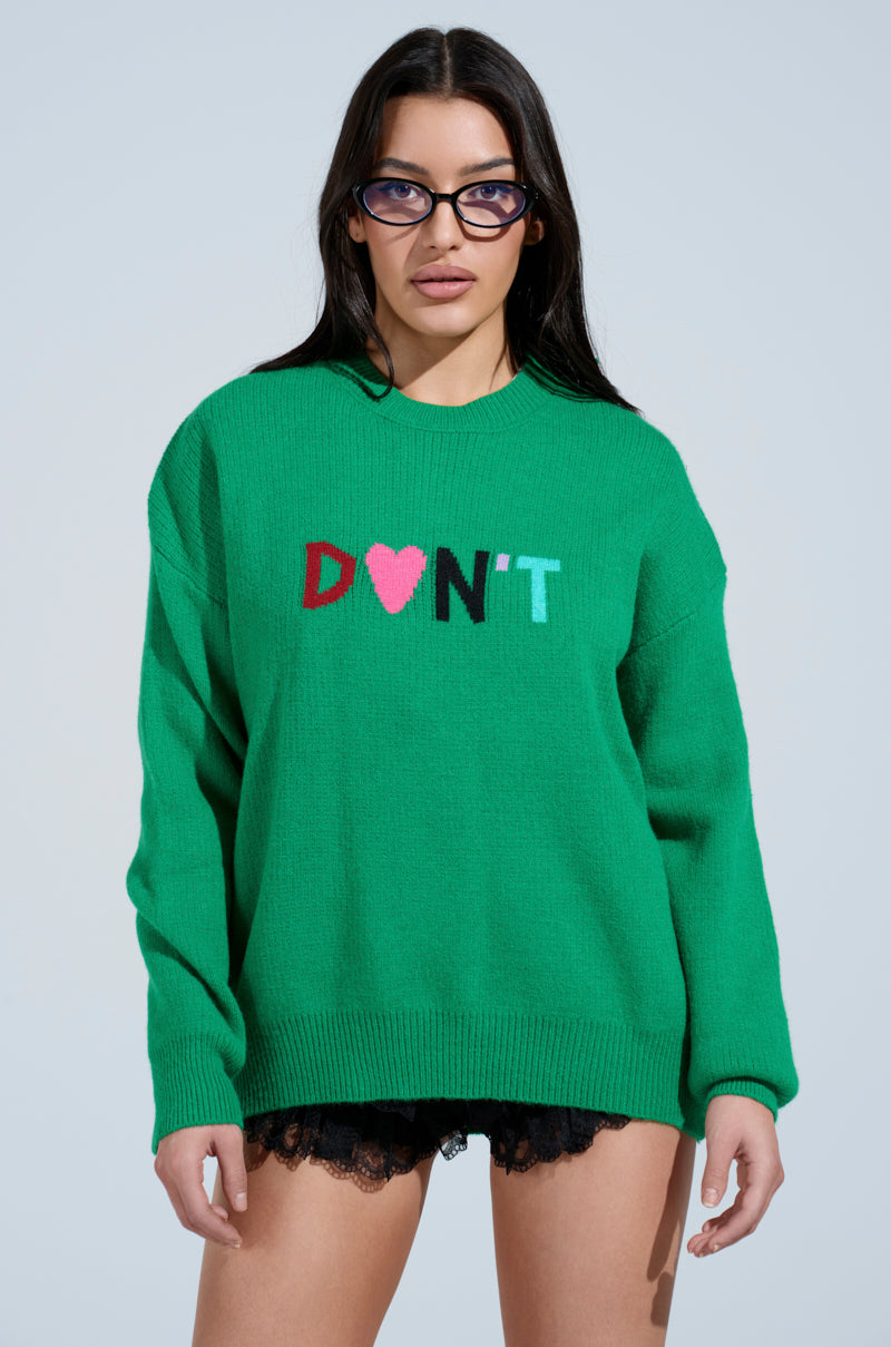 Wearing an AKIRA Label DONT DO IT SWEATER with colorful "DON'T" letters and a heart, paired with black lace shorts, a person with long dark hair and glasses stands against a light blue backdrop.