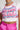 A person wearing the white cropped fit LOVER GIRL BABY TEE featuring pink graffiti-style text and small hearts. They pair the top with vibrant pink pants and accessorize with a sparkly, rhinestone choker.