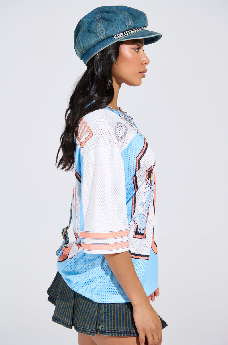Wearing a colorful FLY AWAY JERSEY with sporty stripes and designs, a person in profile stands against a light background. They sport a denim cap and striped mini skirt, with their long hair flowing effortlessly down their back.
