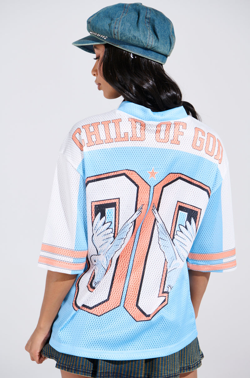 A person in a denim cap and the FLY AWAY JERSEY, showcasing "CHILD OF GOD" and the number 00 with wing graphics and sporty stripes, looks to the side with their hair down.