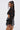 A woman with long, straight hair in a high ponytail wears the AKIRA Label THOUGHT YOU KNEW CROPPED FRINGE TOP and a high-waisted plaid mini skirt with a large bow, standing sideways and looking over her shoulder.