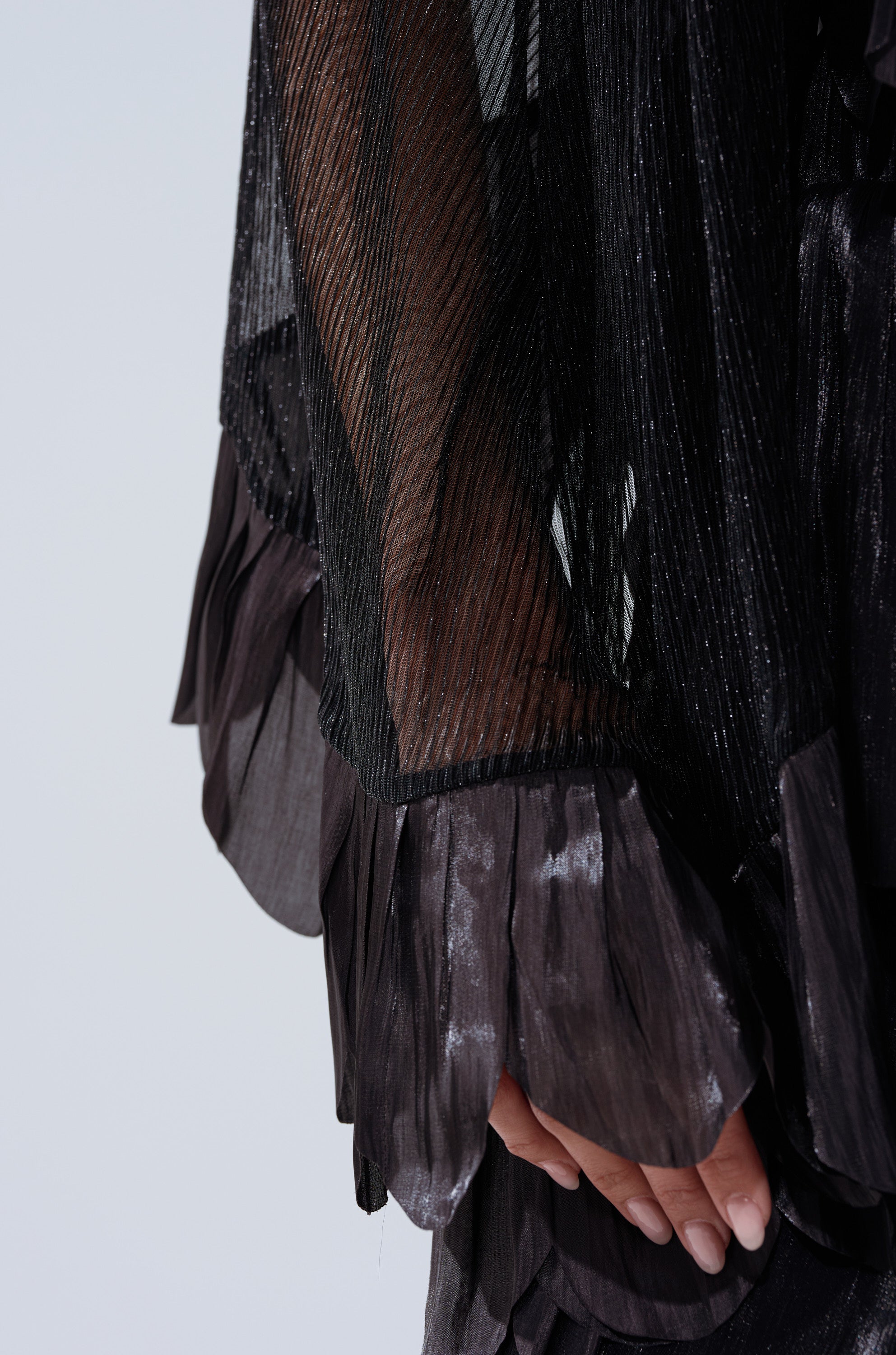A close-up of a hand partially covered by the BRIGHT LIFE BLOUSE with sheer plissé fabric and layered ruffled cuffs, set against a light, neutral background.