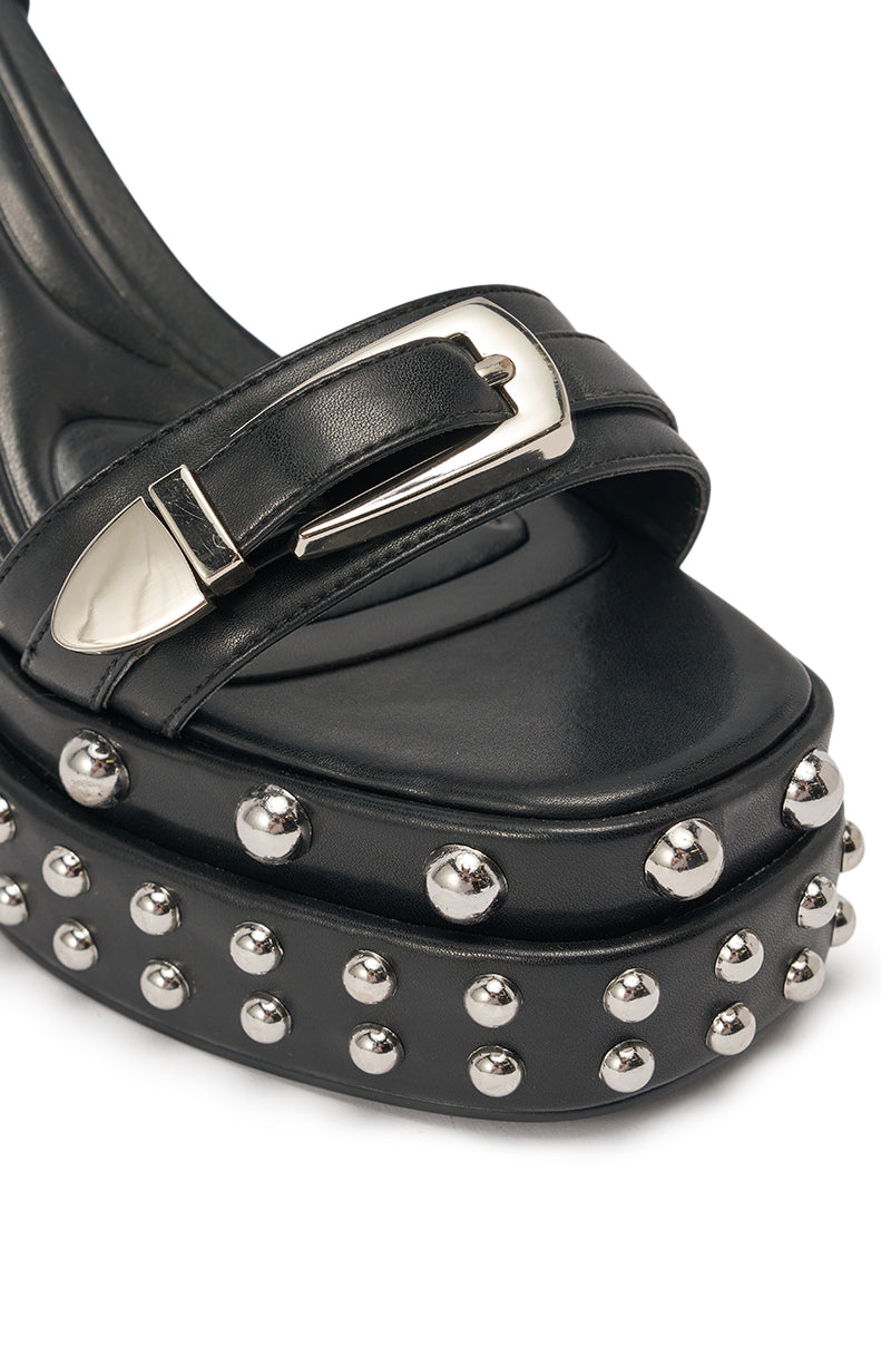 Close-up of the AZALEA WANG EUGENIJA Black Chunky Embellished Studded Sandal, featuring a black faux leather upper, platform sole, silver buckle strap, and metallic studs on the thick block heel. 6