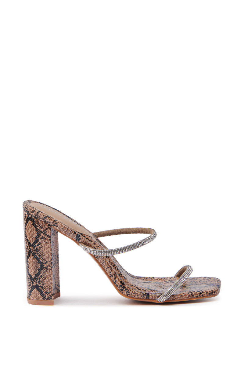 The AZALEA WANG Eulalia Snake Slip On Sandal features a stunning snake print, rhinestone-adorned straps, a chunky block heel, and a squared open toe, offering a bold and stylish side view.