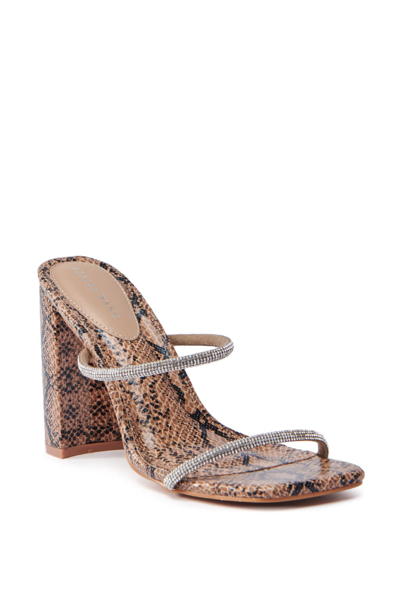The AZALEA WANG EULALIA SNAKE SLIP ON SANDAL features a stylish brown snakeskin pattern and rhinestone straps, complemented by a chunky block heel and open toe design, presented against a white background.