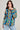 A person with long dark hair poses confidently, wearing the VINTAGE COOL OVERSIZED MULTI COLOR SWEATER paired with blue jeans. They have large hoop earrings and hold the sweater collar with one hand against a plain, light-colored background.
