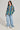A person confidently stands against a neutral background, wearing the VINTAGE COOL OVERSIZED MULTI COLOR SWEATER, paired with baggy light blue jeans and white sneakers. They have long hair adorned with large hoop earrings and layered necklaces.