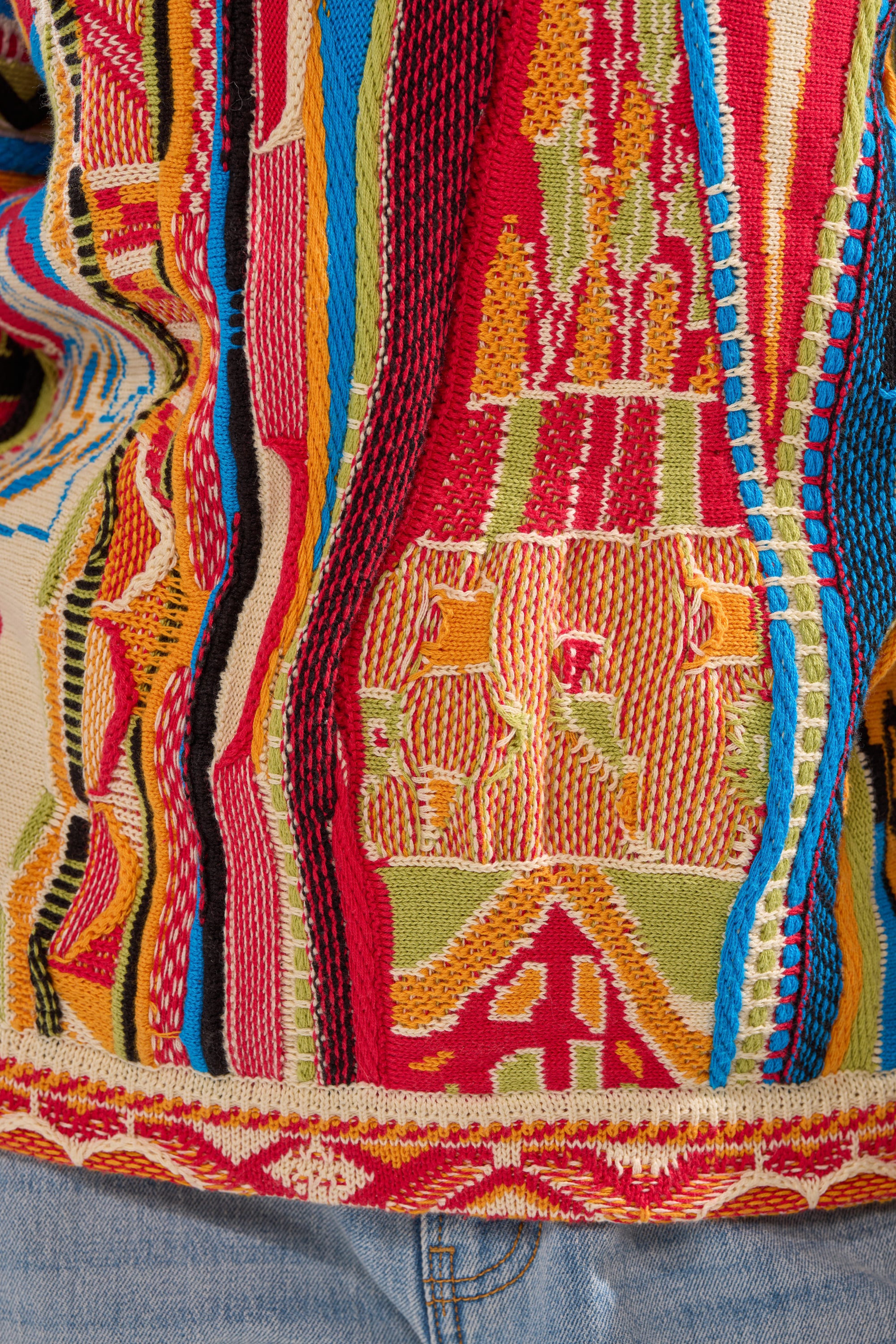 Close-up of the RETRO OVERSIZED SWEATER IN MULTI, featuring vibrant cotton with intricate geometric and abstract patterns in red, yellow, green, blue, and orange, styled over blue denim.