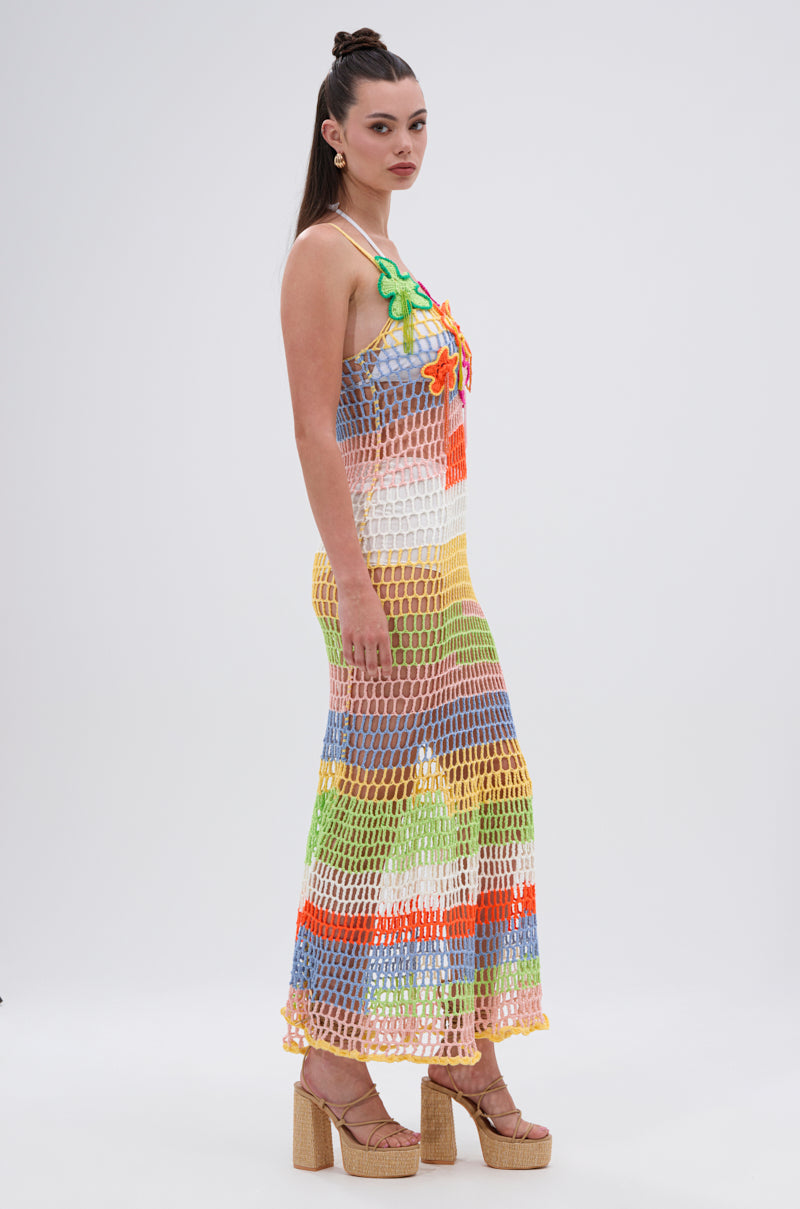 A woman models the BEACHIN IT CROCHET BEADED MAXI DRESS—colorful crochet with floral beading over a white swimsuit—styled with long straight hair, hoop earrings, and platform sandals against a plain white background.