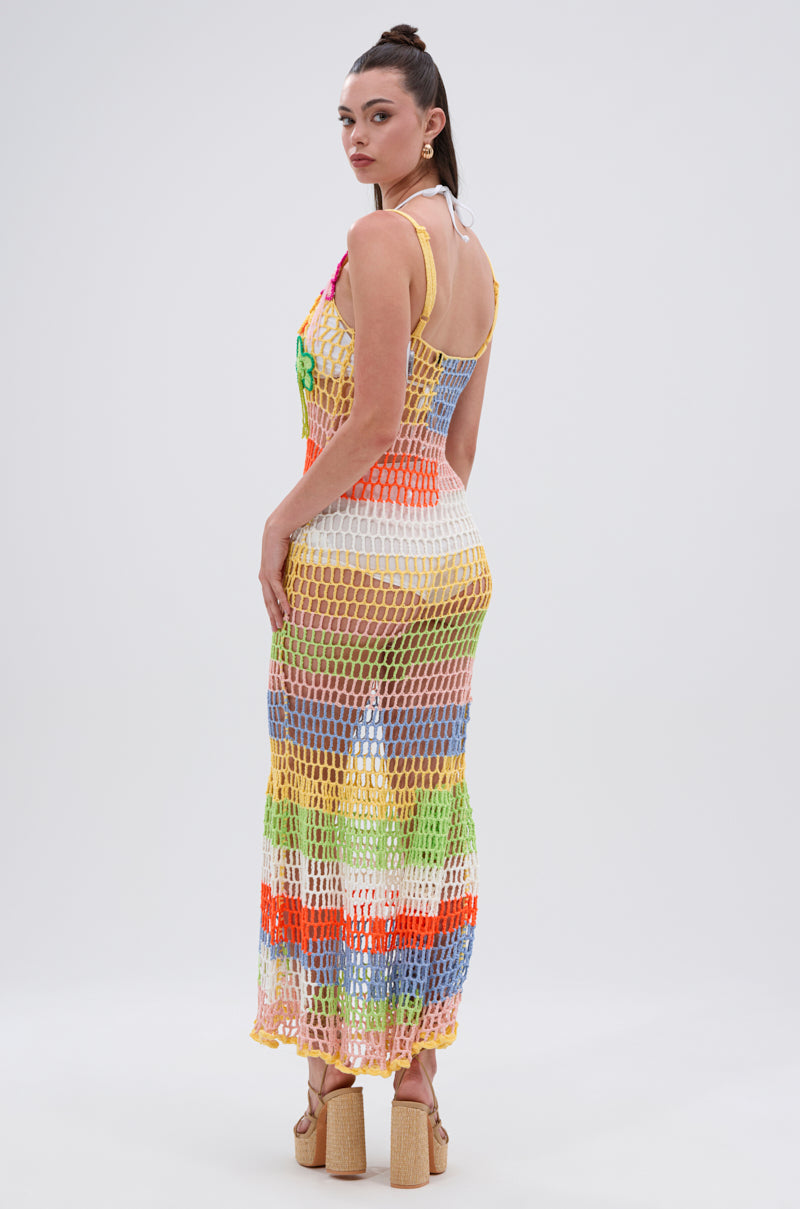 A woman models the BEACHIN IT CROCHET BEADED MAXI DRESS over a white bikini, paired with platform sandals. Her hair is in a high ponytail, and she poses against a plain, light background.